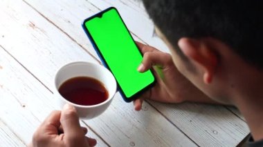 Akıllı telefonu tutan ve çay içen bir adamın en iyi görüntüsü. 