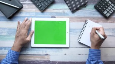 Dijital tablet kullanan ve not defterine yazı yazan işadamlarının üst görünümü 