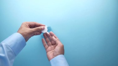 Genç adam mavi arka planda dezenfektan jeli kullanıyor. 