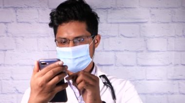 Koruyucu maskeli doktor hastanede akıllı telefon kullanıyor..