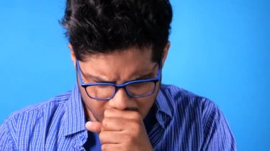  Genç adam öksürüyor ve mavi arka planda hapşırıyor. 