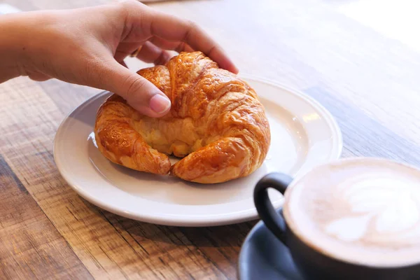 Vrouwen hand houden croissant op houten tafel — Stockfoto