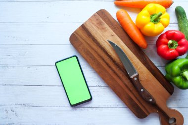 Taze sebzeler, kesim tahtası ve masada akıllı telefon. 