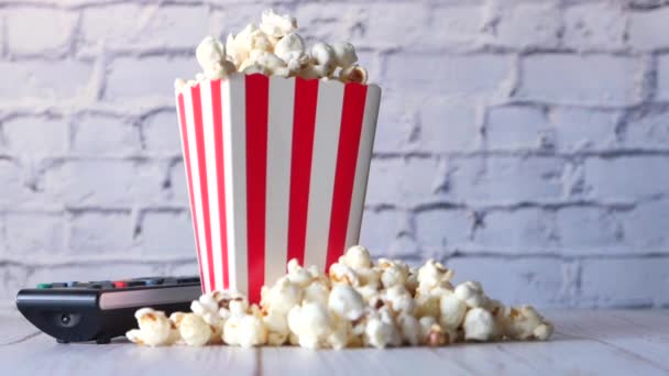 Primer plano de palomitas de maíz en un contenedor y control remoto de televisión en la mesa — Vídeos de Stock