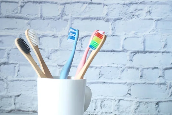 Cepillos de dientes coloridos en taza blanca contra una pared — Foto de Stock