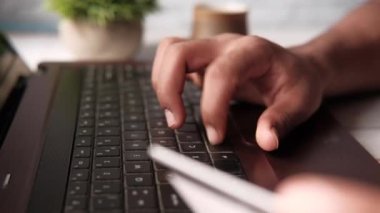 Adamın elleri kredi kartını tutuyor ve internetten bilgisayar alışverişi yapıyor. 
