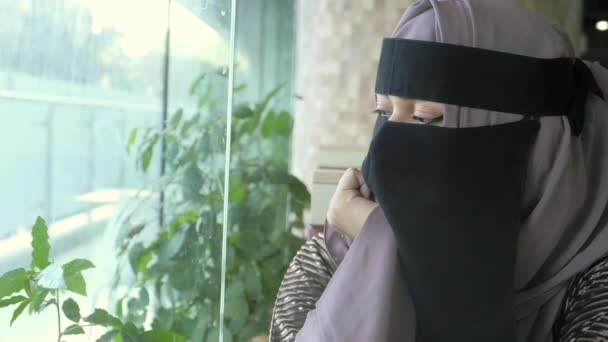 Молоді мусульманські жінки, що закривають обличчя, дивляться через вікно в приміщенні — стокове відео