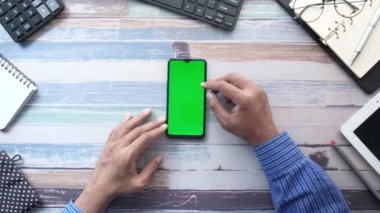 Ofis masasında akıllı telefon kullanan bir adamın üst görüntüsü. 