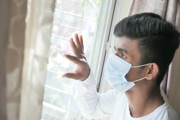 Mladý muž s ochrannou maskou, dívající se oknem. — Stock fotografie