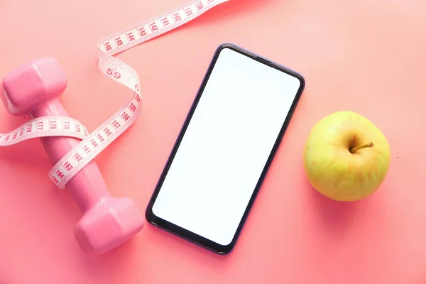 Conceito de dieta saudável com telefone inteligente, maçã e haltere no fundo rosa — Fotografia de Stock