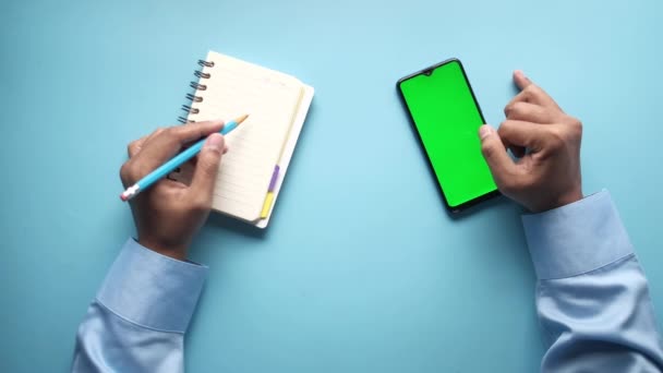 Человек руку со смартфоном и писать на блокноте — стоковое видео
