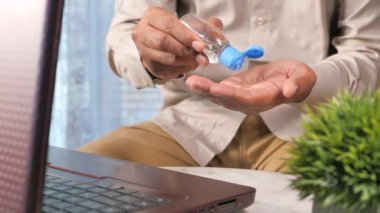  Genç adam ofis masasında dezenfektan jeli kullanıyor. 