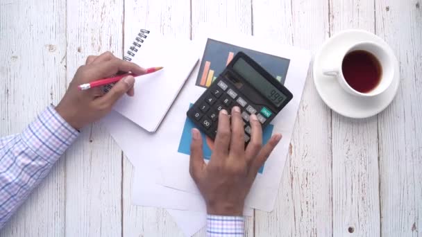İnsan elinin hesap makinesi kullanarak ve not defterine yazarak en üst görünümü — Stok video