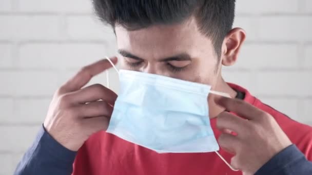 Молодий азіатський чоловік кладе хірургічну маску для обличчя в приміщенні — стокове відео
