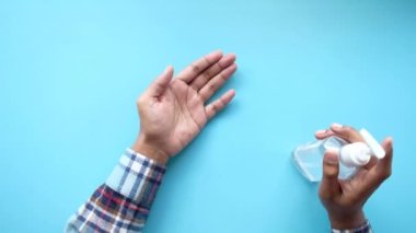 Mavi arka planda virüsü önlemek için dezenfektan jel kullanan bir adamın en üst görünümü 