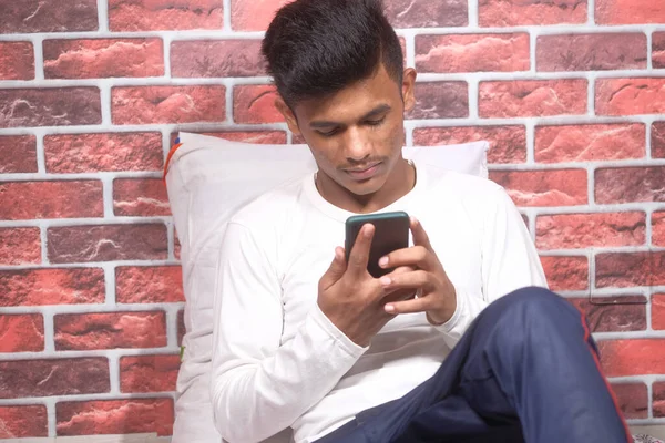 Joven acostado en la cama usando un teléfono inteligente. — Foto de Stock