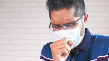  Tıbbi maskeli genç adam öksürüyor ve hapşırıyor. 