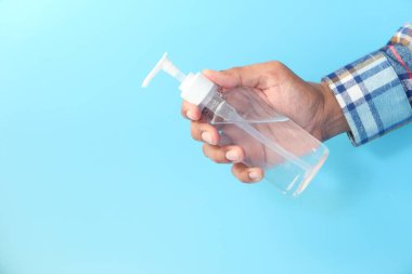 Delikanlının mavi arka planda dezenfektan jeli tutuşu. 