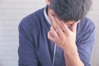 Genç adam baş ağrısı çekiyor ve yüzünü eliyle örtüyor. 