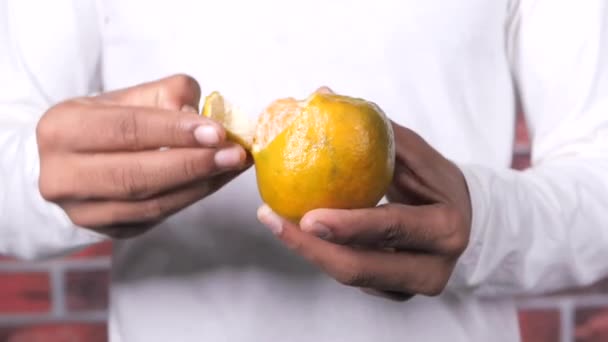 Joven sacando la piel de una fruta naranja — Vídeos de Stock