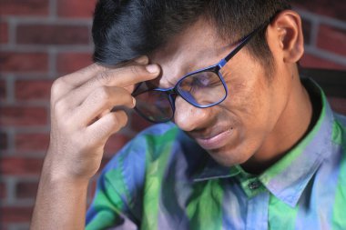 Genç adam sandalyede otururken baş ağrısı çekiyor. 