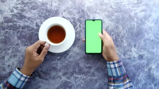 Вид сверху на человеческую руку с помощью смартфона и питьевого чая — стоковое видео