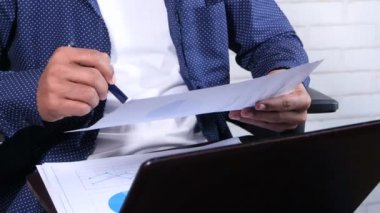 Genç adam bir sandalyede oturmuş kağıt üzerinde finansal verileri analiz ediyor. 