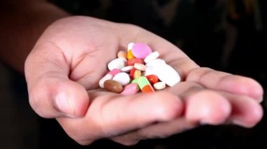 Elinde ilaç hapları ve siyah kapsül olan adamlar var. 