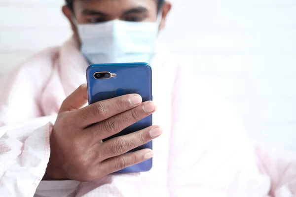 Yüzünde cerrahi maske olan hasta adam akıllı telefon kullanıyor, seçici odaklanıyor. — Stok fotoğraf