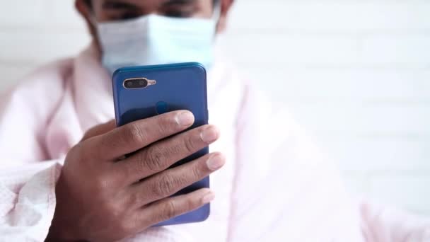 Хворий чоловік у хірургічній масці для обличчя за допомогою смартфона, вибірковий фокус — стокове відео