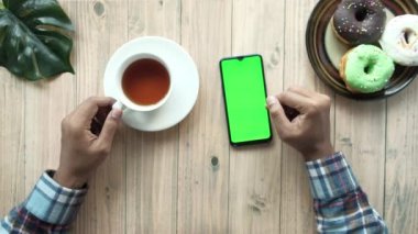 Akıllı telefon kullanan ve masada çay içen bir adamın üst görüntüsü. 