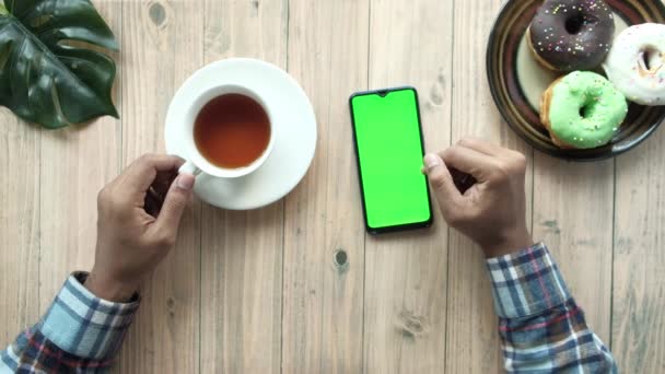 Shora pohled na člověka rukou pomocí chytrého telefonu a pití čaje na stole — Stock video