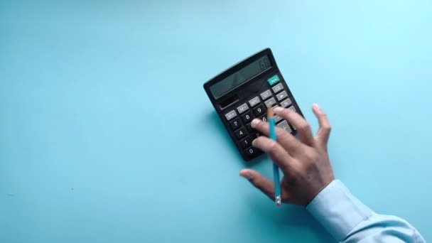 Vista dall'alto della mano dell'uomo utilizzando la calcolatrice su sfondo blu — Video Stock