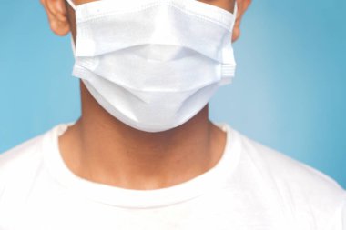 Mavi arka planda koruyucu maskeli genç bir adam. 