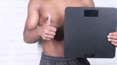 Ağırlık makinesi tutan genç adam başparmak işareti yapıyor. 