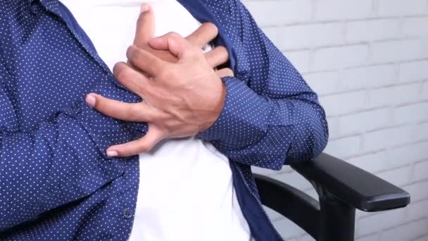 Νεαρός άνδρας που κάθεται στην καρέκλα και υποφέρει από πόνο στην καρδιά και κρατώντας το στήθος με το χέρι — Αρχείο Βίντεο