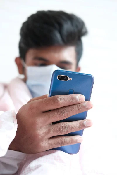 Yüzünde cerrahi maske olan hasta adam akıllı telefon kullanıyor, seçici odaklanıyor. — Stok fotoğraf