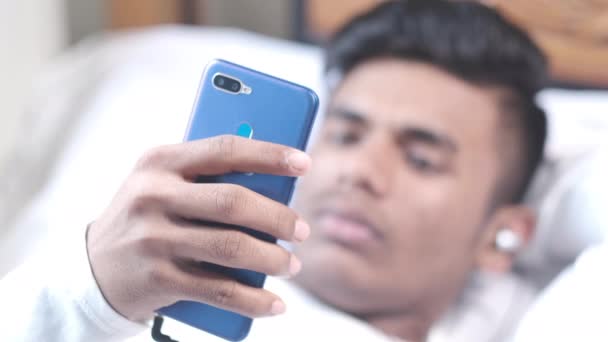 Vzrušený mladý muž na posteli pomocí chytrého telefonu v noci — Stock video