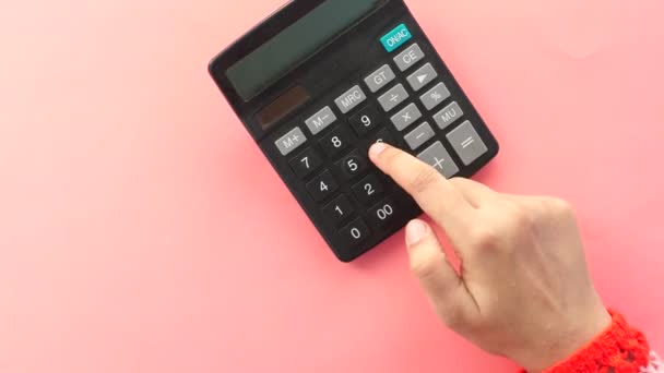 Mulheres mão usando calculadora no fundo rosa, de cima para baixo — Vídeo de Stock