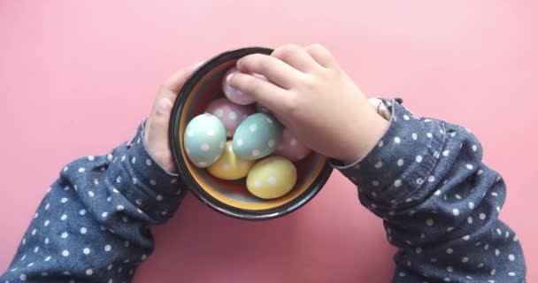 Main d'enfant tenant un bol d'œufs de Pâques sur rose — Video