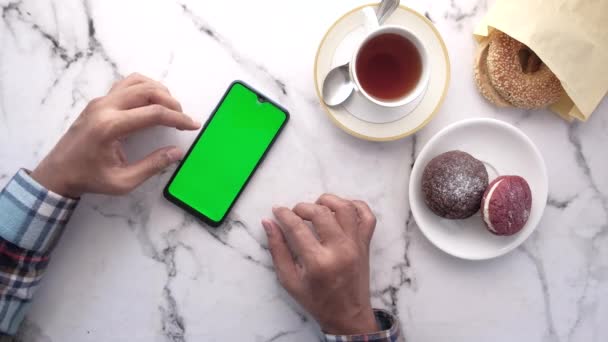 Вид сверху на руку человека с помощью смартфона с чаем и печеньем на столе — стоковое видео