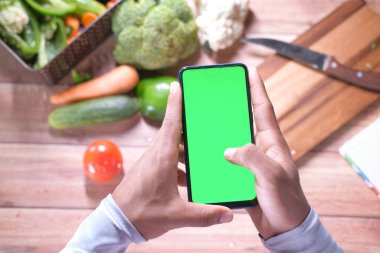 Arka planda akıllı telefon ve sebze kullanan genç adamın üst görünümü 