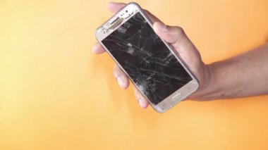 Kırık akıllı telefonu turuncu arka planda tutan adamın elini yakın plan 