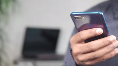 Arka planda akıllı telefon ve dizüstü bilgisayar kullanarak genç adamın elini kapat 