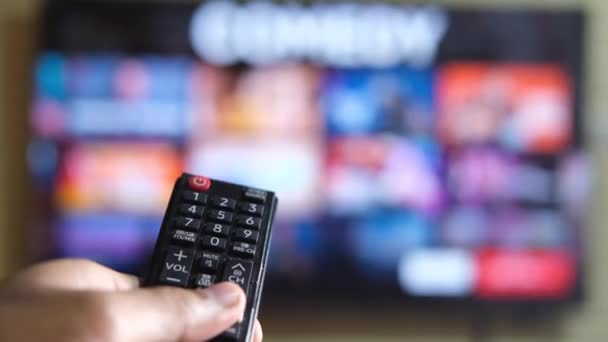 Κοντινό πλάνο του ανθρώπου χέρι κρατώντας τηλεχειριστήριο τηλεόραση και βλέποντας τηλεόραση — Αρχείο Βίντεο