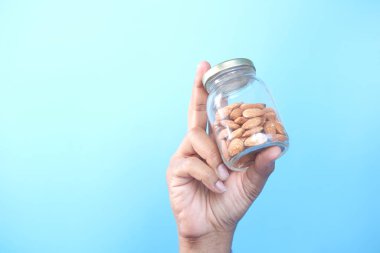  Mavi arka planda bir kavanoz badem fıstığını tutan el. 