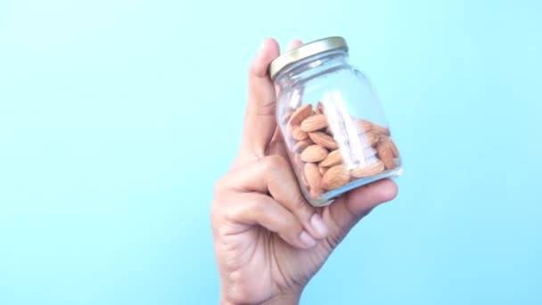 Hand holding a jar of almond nuts against blue background — Stock Video