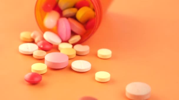 Gros plan de nombreuses pilules et capsules colorées se répandant sur fond orange — Video