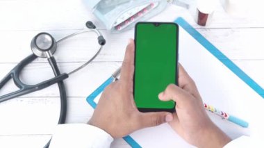 Üst düzey erkek doktor, klinik masasında akıllı telefon kullanıyor.