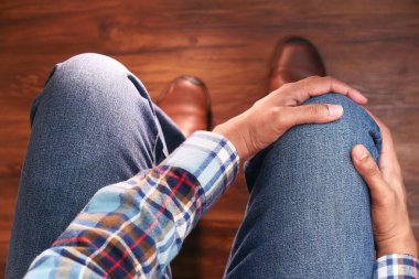 Bir sandalyede oturan bir adamın diz eklem ağrısı çekmesi. 